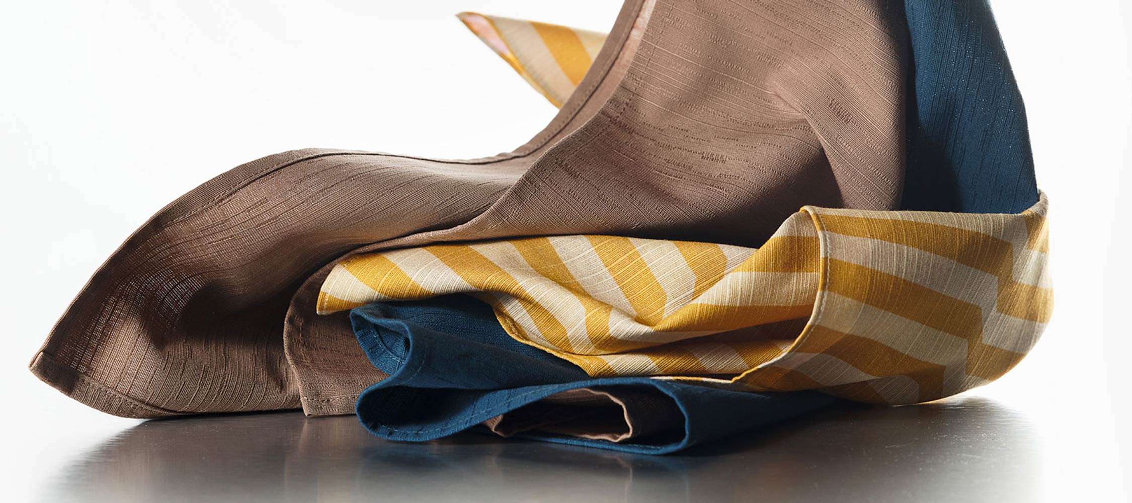 Folded cloth napkins in brown, denim, and golden stripe.