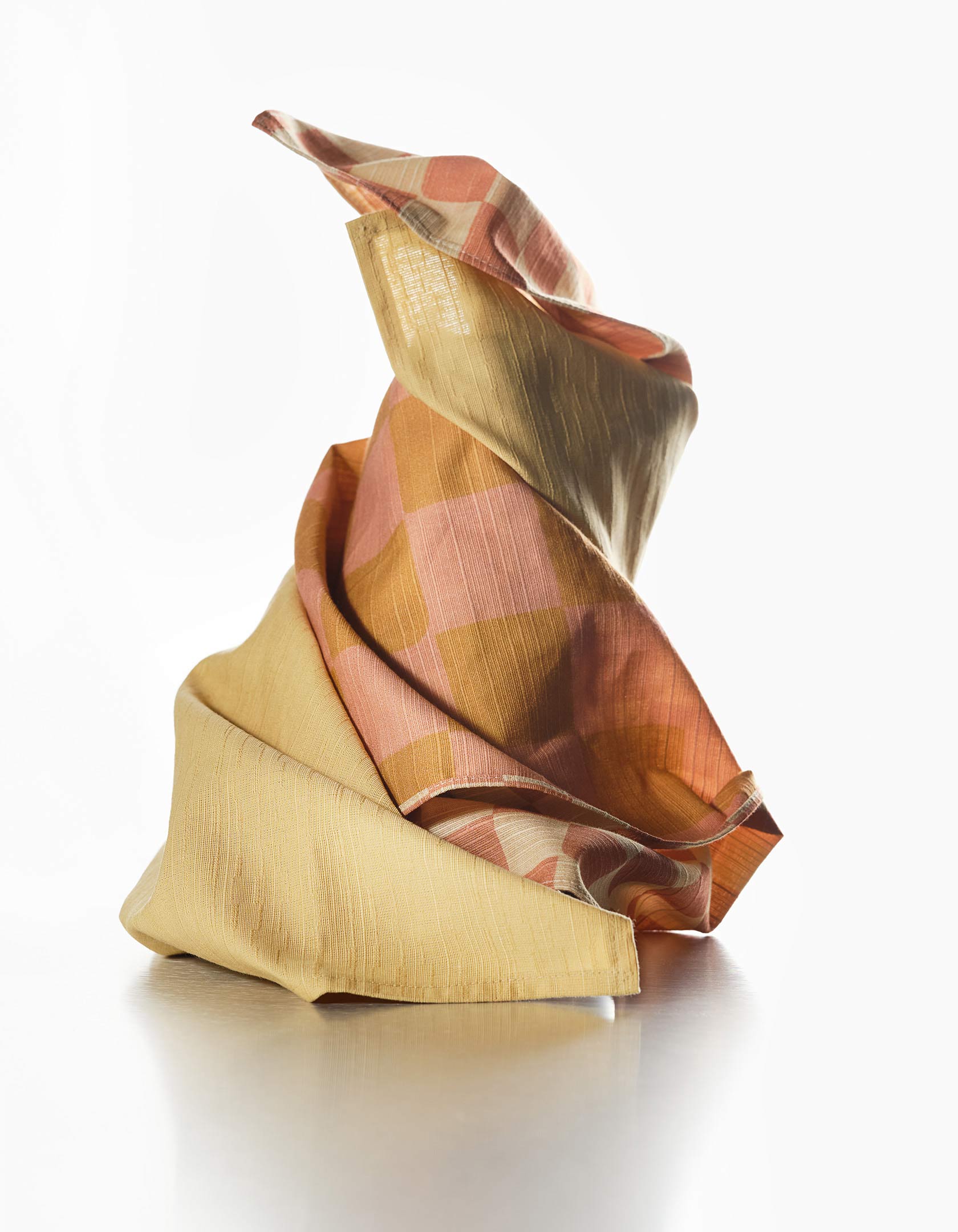 Twisted dinner napkins with a checkered pattern in shades of brown, yellow, cream, and pink 